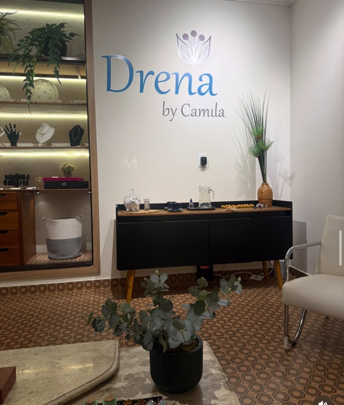 Recepção da Drena by Camila, com o logotipo azul na parede, aparador, plantas e vitrine iluminada